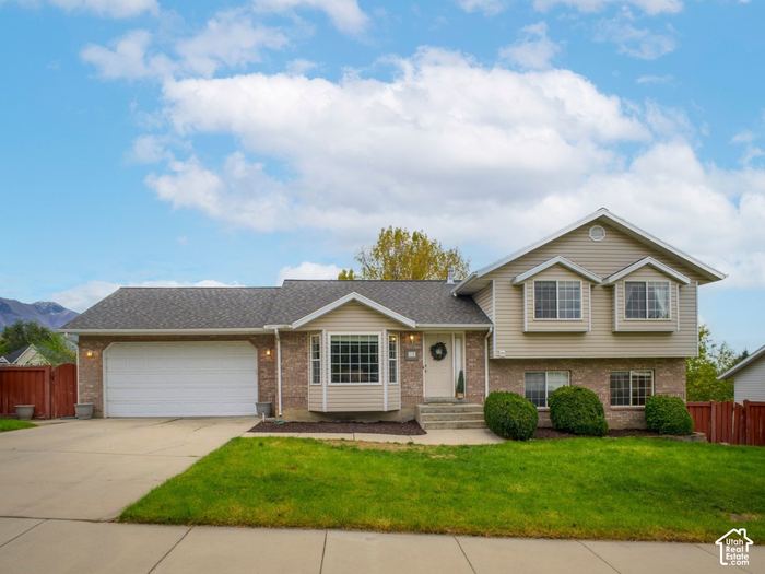 Front of the house with a 2-car garage, brick accents, and a green lawn